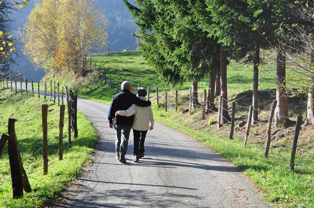 An older couple walking arm in arm down a country lane